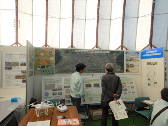地区の航空写真の前で事業概要を説明する様子