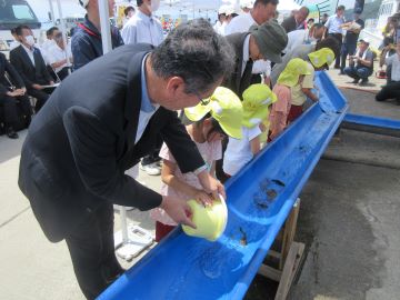  稚魚を放流する園児と朝倉地方参事官