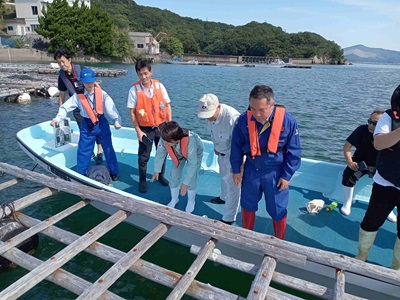 船上でカキ養殖いかだの被災状況の説明を受ける山本農林水産大臣政務官(中央)