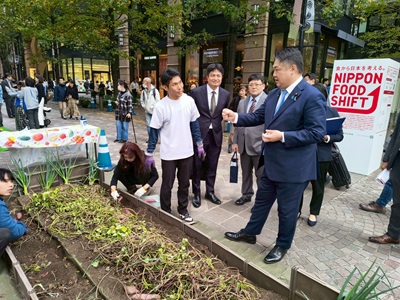 「NIPPON FOOD SHIFT FES.東京2025」の収穫体験ブース出展者から説明を受ける山本農林水産大臣政務官
