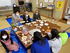 集会所で７人で集まってごはんを食べている様子