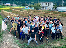 天日干しした稲をバックにした集合写真