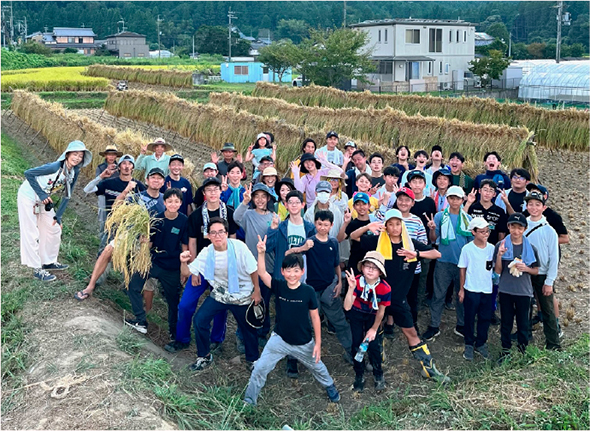 天日干しした稲を背景に子供と大人が集合してピースをする。