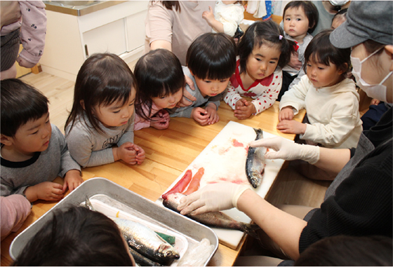 ニシンを捌く人とその様子を見つめる子供たち