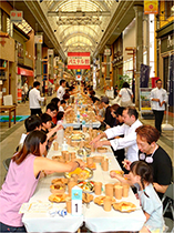 商店街で大勢の人がともにご飯を食べる様子