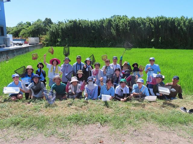 田んぼの前で網を持っている集合写真