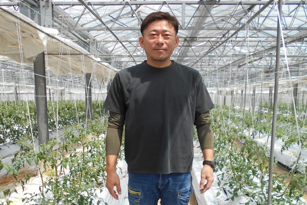 ビニールハウスの中で生産者が立っている