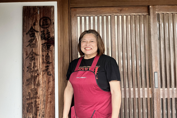 酢の店の前で女主人がたっている