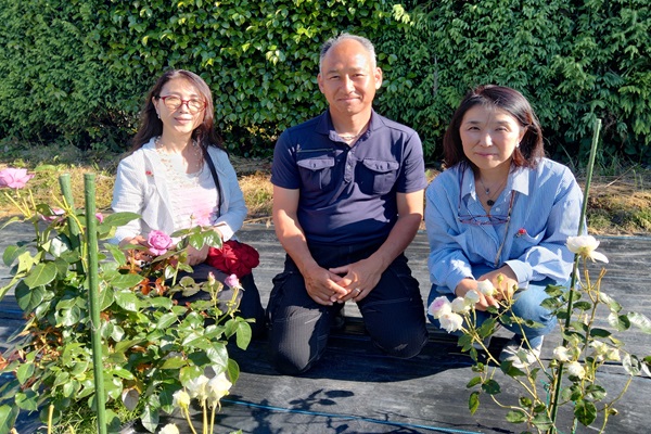 バラが咲き誇る前で3人