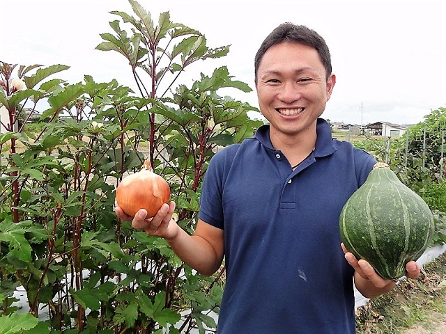 農場の前で収獲した野菜を持つ野口さん