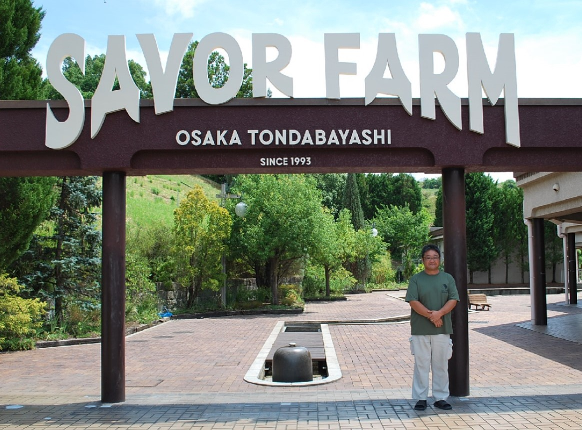 ゲートに立つ富田林市南地区協同組合本間副理事長