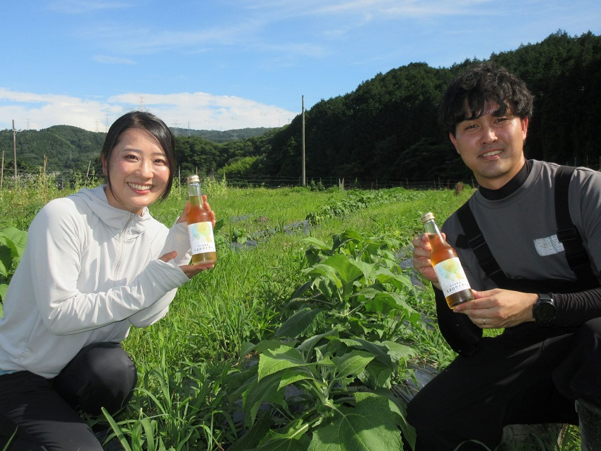 ヤーコン畑で「とよのサイダー」を手にする森下さんと浅野さん