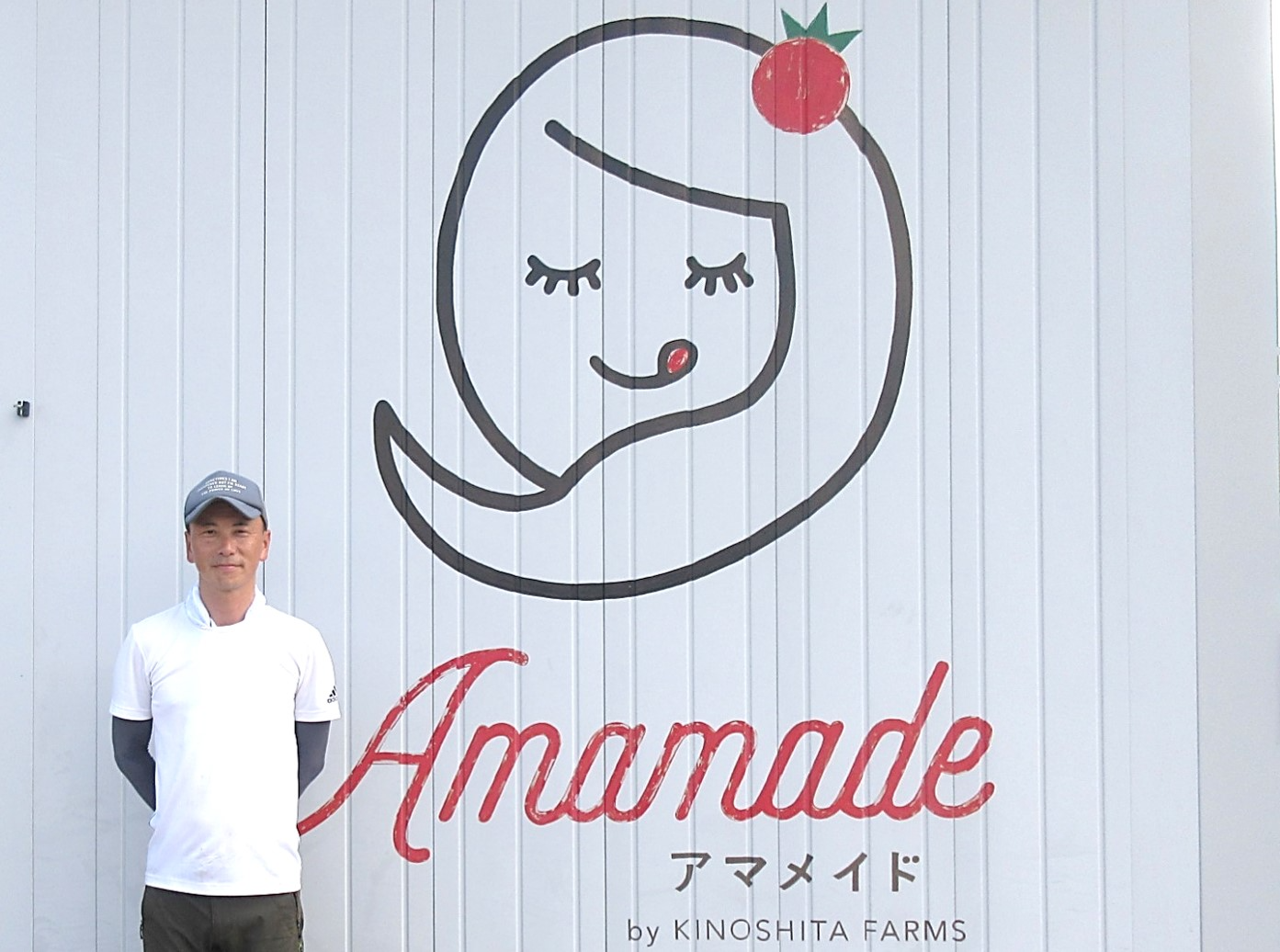 自社ブランド名の入った会社入口に立つ木下代表