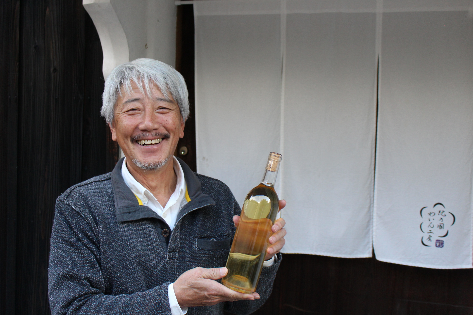 紀乃國わいん工房の南口さんが今年度完成した和歌山県（自社畑）産のぶどうのみで作られた白ワインを持って立っている