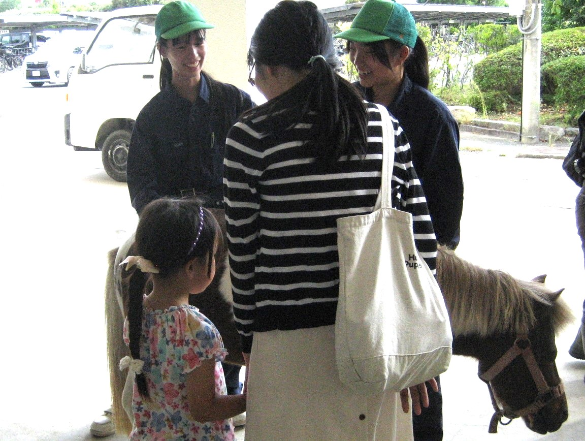 生徒が連れたポニーとふれあう親子の買い物客