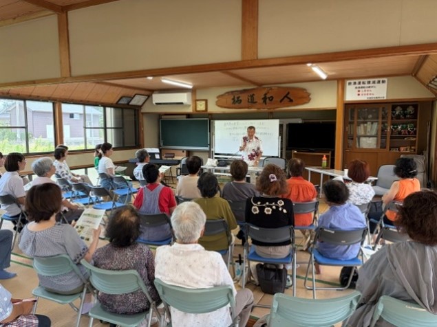 地域の集会室で講師が高齢者を中心とした参加者約20名に向けて講演を行っている様子