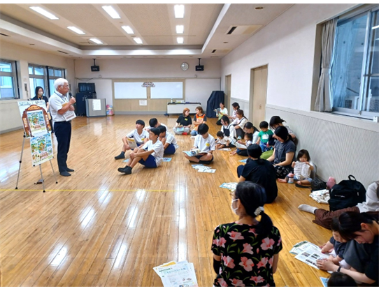 前方で紙芝居を使って話しています。子どもたちは近くで話を聞いています。