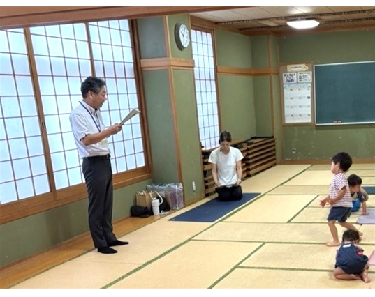 公民館の和室に親子や学生が集まり、職員の説明を聞いています。