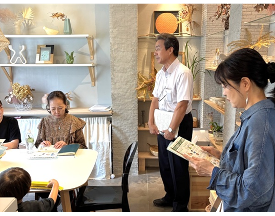 座学冒頭に、消費者として取り組んでほしいことを説明する職員と、説明資料を見る伊藤香菜子さんと参加者