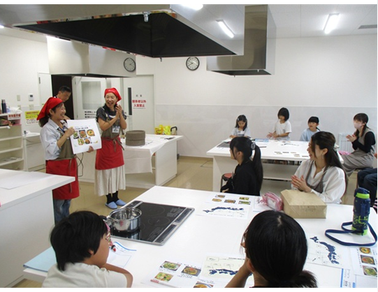 調理室で、講師から料理や食材について説明を受けています。
