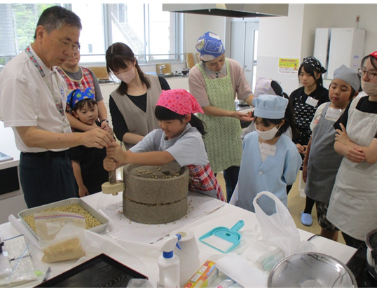 子どもたちが石うすを使い、大豆をひいてきな粉作っている様子です。