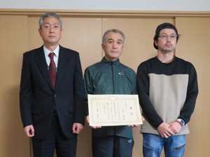 賞状を手にする福士さん（中央）とご子息（右）、齋藤参事官