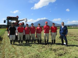 岩手山とコンバインをバックに並ぶ高校生６人と関係者