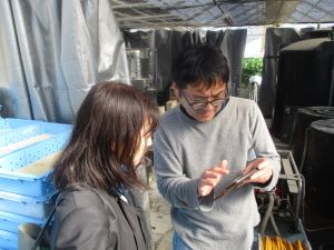 スマートホンを使用した環境制御システムの説明を受ける長田地方参事官（左）