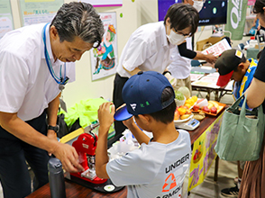 山形県拠点の情報発信ブース（缶バッジ作製（手前）、フルーツ重さ当てクイズ（奥））