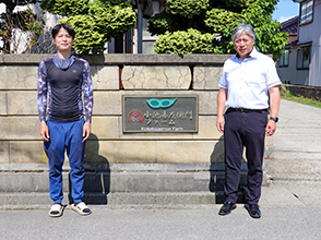 会社の看板前にて 左側が小池貴士氏、右側が花田地方参事官