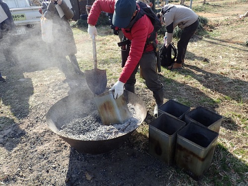 炭化した剪定枝を一斗缶に投入し蓋をして消化する作業風景（令和7年2月7日撮影）
